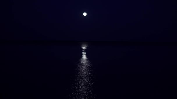 La pleine lune est suspendue très bas au-dessus de l'horizon dans une mer très calme deux heures avant l'aube. Le chemin lunaire s'étend le long de toute la mer jusqu'à la côte