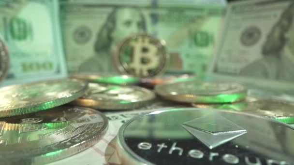 Mata uang Blockchain di atas meja dengan banyak dolar AS dalam lampu hijau. Kamera bergerak ke koin utama Bitcoin dari perak Etherium. Tembakan makro sudut rendah — Stok Video