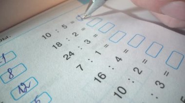 Öğrenci çarpma örneklerini çözer. Çocuk elinde siyah bir kalem tutuyor ve cevaplar yazıyor. Çarpım tablosu örnekleriyle dolu bir defter. Çarpım tablosu öğretiliyor
