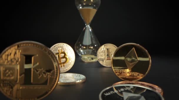 Mange gull-krypto-mynter på den svarte overflaten Bitcoin, Etherium, Litecoin. Hannhånden vender timeglasset. Tid er penger. Bitemynt er den digitale hovedverdien – stockvideo