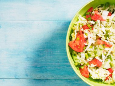 Yeşil fincanda salata için dilimlenmiş sebzeler. Beyaz ve mavi ahşap arka planda.