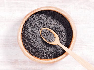 Tahta zemin üzerinde kahverengi ahşap fincanda siyah susam (susam) ve kaşık.