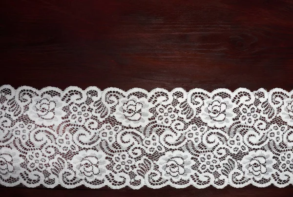Bílá široká krajka na tmavohnědém dřevěném pozadí — Stock fotografie