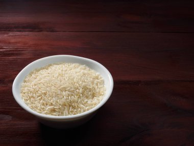 Kahverengi ahşap arka planda beyaz bir kâse içinde çiğ Basmati pilavı.