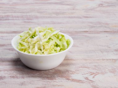 Tahta arka planda beyaz bir kasede doğranmış yeşil lahana.