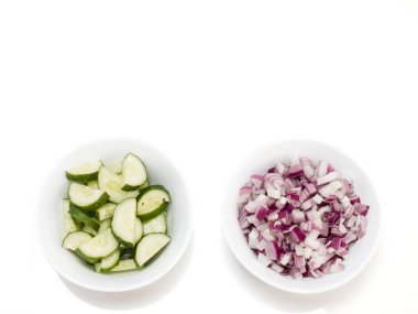Beyaz arka planda beyaz kaselerde dilimlenmiş kırmızı soğan ve salatalıklar.