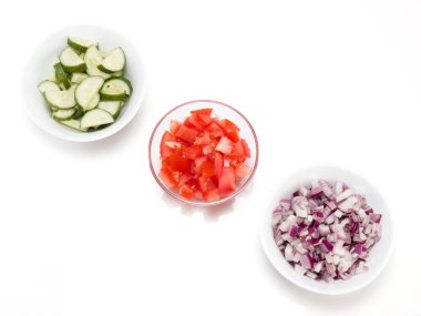 Şeffaf bir kasede dilimlenmiş domates, beyaz arka planda kırmızı soğan ve salatalıklar.