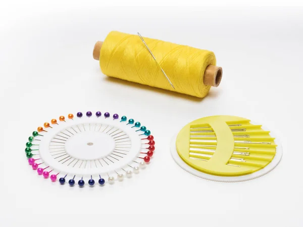 Bobina con hilos amarillos con una aguja, un juego de alfileres y aguja, sobre un fondo blanco —  Fotos de Stock