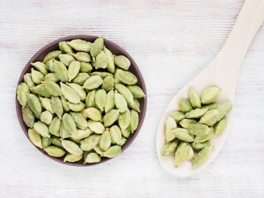 Baharat yeşili kakule (Elettaria kakule) kahverengi ahşap arka planda bir kaşıkla kilden bir tabakta