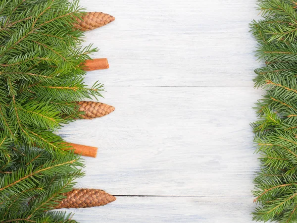 Fir tree branch with cones, cinnamon on white wooden background.