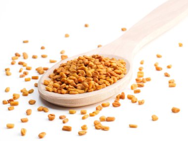 Diagonal wooden (Trigonella) spoon with fenugreek on a white bac