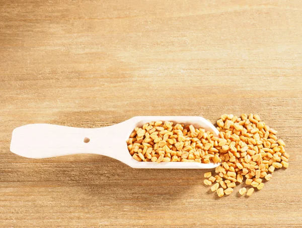 Fenegriek (Trigonella) in een houten bolletje op een houten ondergrond — Stockfoto