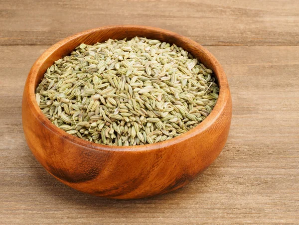 Fennel seeds (Foeniculum vulgare) in a wooden cup on a wooden ba