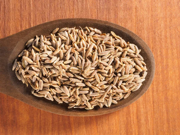 Семена кумина (Cuminum), Джира в деревянной ложке на коричневом дереве — стоковое фото