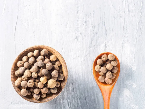 Allspice (pimenta da Jamaica) em uma xícara de madeira e colher em uma ba cinza — Fotografia de Stock