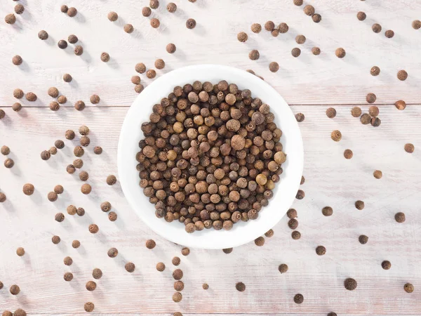 Piment (Jamaica-Pfeffer) in einer weißen Tasse auf einem hölzernen braunen Backblech — Stockfoto