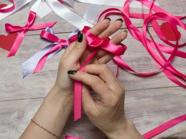 Genç kadın, ahşap bir sırtındaki pembe saten kurdelenin yaylarını bağlıyor.