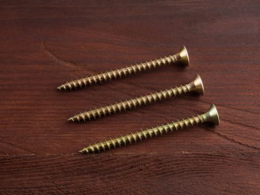 Kahverengi ahşap arka planda üç uzun metal vida