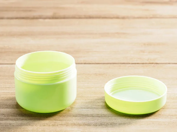 Zelený kelímek pro kosmetické výrobky s otevřeným víčkem izolovaným na dřevě — Stock fotografie