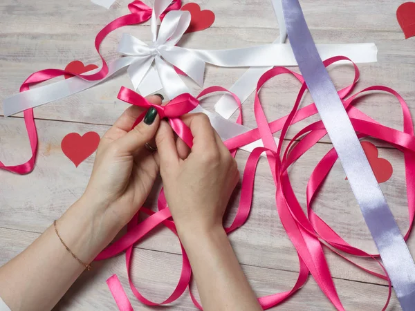 Woman ties a knot with two bows of pink satin ribbon. Scrapbooki