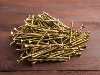 Kahverengi ahşap arka planda uzun metal vidalar var. Endüstriya