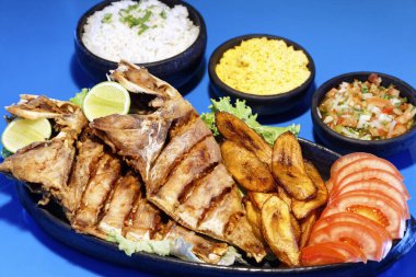 Domates, limon, pirinç, farofa ve sirke ile servis edilen kızarmış balık.