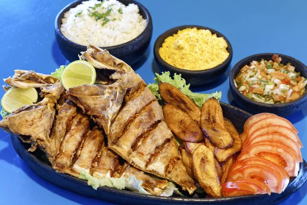 Domates, limon, pirinç, farofa ve sirke ile servis edilen kızarmış balık.