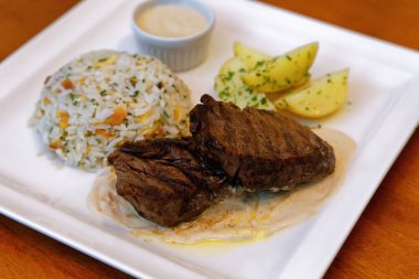 Peynir soslu fileto, bitkilerle birlikte pirinç, kabak çekirdeği ve patates sotesi.