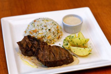 Peynir soslu fileto, bitkilerle birlikte pirinç, kabak çekirdeği ve patates sotesi.