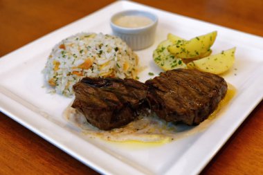 Peynir soslu fileto, bitkilerle birlikte pirinç, kabak çekirdeği ve patates sotesi.