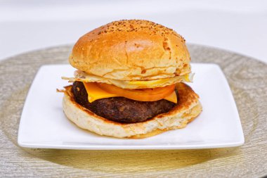 Lezzetli pastırmalı çizburger, peynirli, kızarmış yumurta ve et, beyaz tabakta servis edilir..