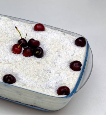 Cam bir tabakta hindistan cevizli vişneli turta, taze kirazlarla süslenmiş.