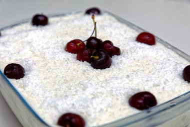 Cam bir tabakta hindistan cevizli vişneli turta, taze kirazlarla süslenmiş.