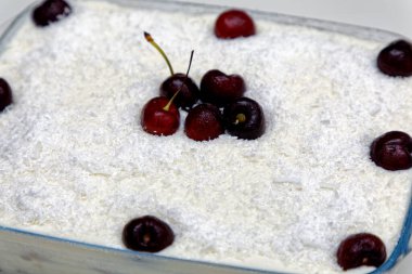 Cam bir tabakta hindistan cevizli vişneli turta, taze kirazlarla süslenmiş.