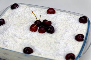 Cam bir tabakta hindistan cevizli vişneli turta, taze kirazlarla süslenmiş.