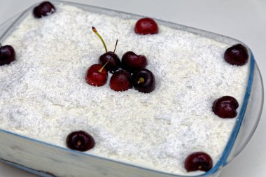 Cam bir tabakta hindistan cevizli vişneli turta, taze kirazlarla süslenmiş.