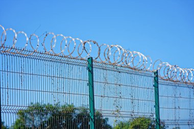 Dikenli tel ve mavi arka planlı güvenlik çiti