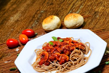 Domuz pastırmalı ve şampiyon soslu tam tahıllı spagetti fesleğenle süslenmiş ve yanında patates ekmeği ve vişneli domates..