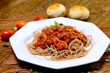 Domuz pastırmalı ve şampiyon soslu tam tahıllı spagetti fesleğenle süslenmiş ve yanında patates ekmeği ve vişneli domates..