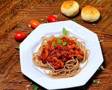 Domuz pastırmalı ve şampiyon soslu tam tahıllı spagetti fesleğenle süslenmiş ve yanında patates ekmeği ve vişneli domates..