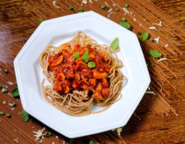 Domuz pastırmalı ve şampiyon soslu tam tahıllı spagetti fesleğenle süslenmiş ve yanında patates ekmeği ve vişneli domates..