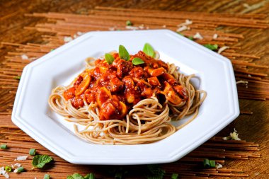 Domuz pastırmalı ve şampiyon soslu tam tahıllı spagetti fesleğenle süslenmiş ve yanında patates ekmeği ve vişneli domates..