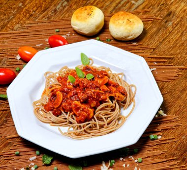 Domuz pastırmalı ve şampiyon soslu tam tahıllı spagetti fesleğenle süslenmiş ve yanında patates ekmeği ve vişneli domates..