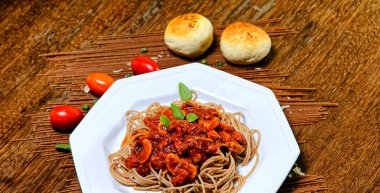 Domuz pastırmalı ve şampiyon soslu tam tahıllı spagetti fesleğenle süslenmiş ve yanında patates ekmeği ve vişneli domates..