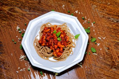 Domuz pastırmalı ve şampiyon soslu tam tahıllı spagetti fesleğenle süslenmiş ve yanında patates ekmeği ve vişneli domates..