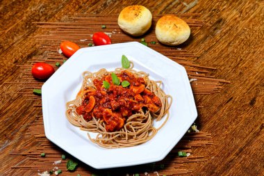 Domuz pastırmalı ve şampiyon soslu tam tahıllı spagetti fesleğenle süslenmiş ve yanında patates ekmeği ve vişneli domates..