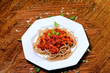 Domuz pastırmalı ve şampiyon soslu tam tahıllı spagetti fesleğenle süslenmiş ve yanında patates ekmeği ve vişneli domates..