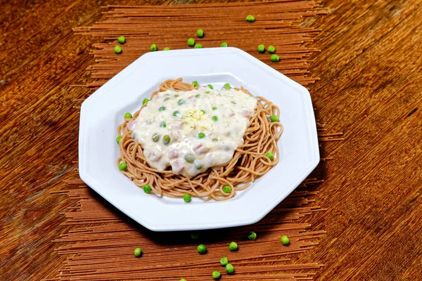 Wholegrain spaghetti in white sauce with peas and ham