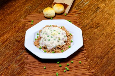 Bezelye ve jambonlu, beyaz soslu tam tahıllı spagetti.