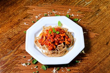 Domuz pastırmalı ve şampiyon soslu tam tahıllı spagetti fesleğenle süslenmiş ve yanında patates ekmeği ve vişneli domates..